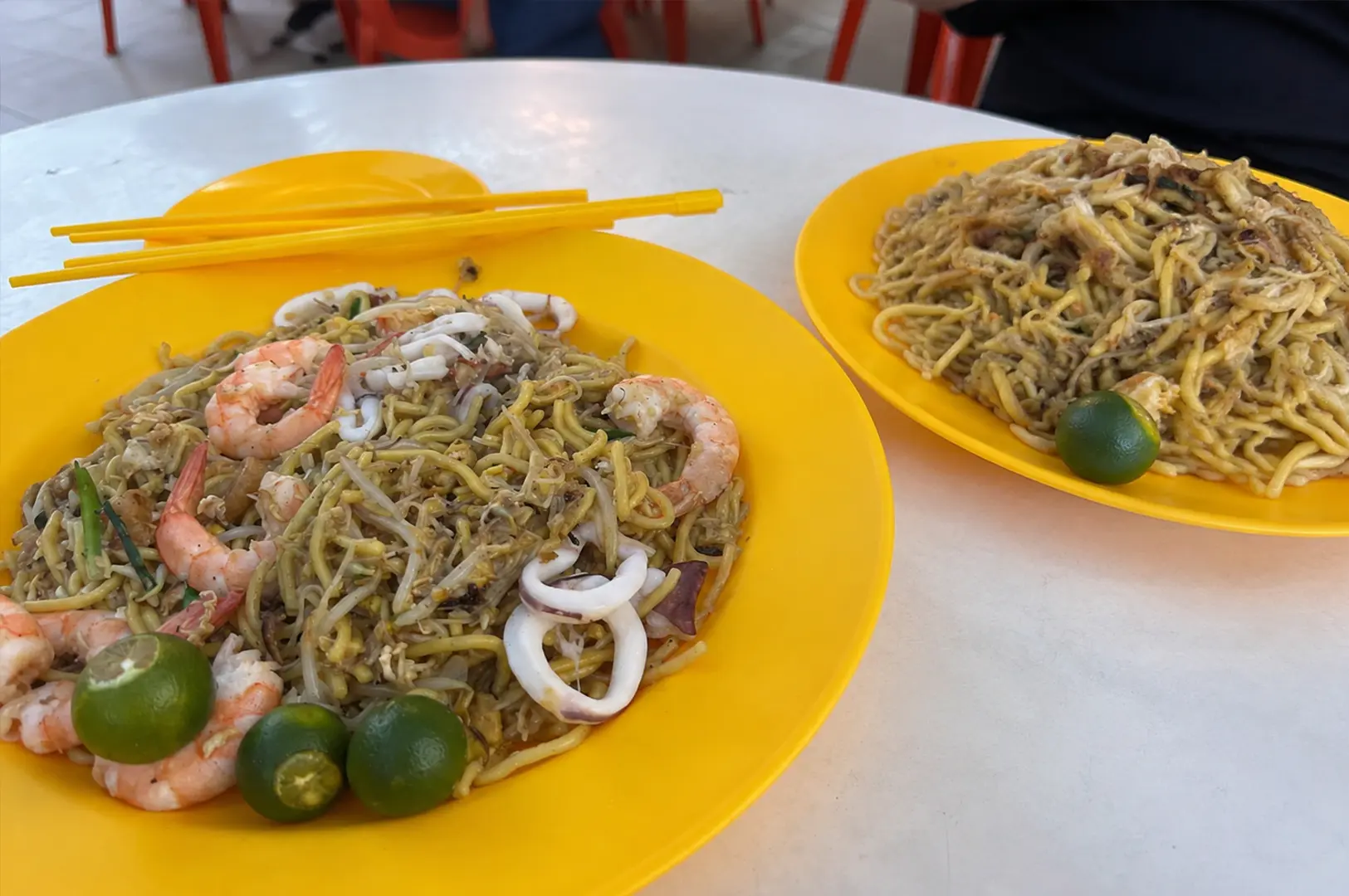 Two plates of Singapore Hokkien mee, including seafood noodles with prawns, squid, bean sprouts and calamansi.