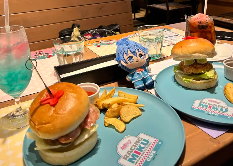 Racing Miku café meal with themed burgers, colorful drinks, and a blue-haired character plush on the table.