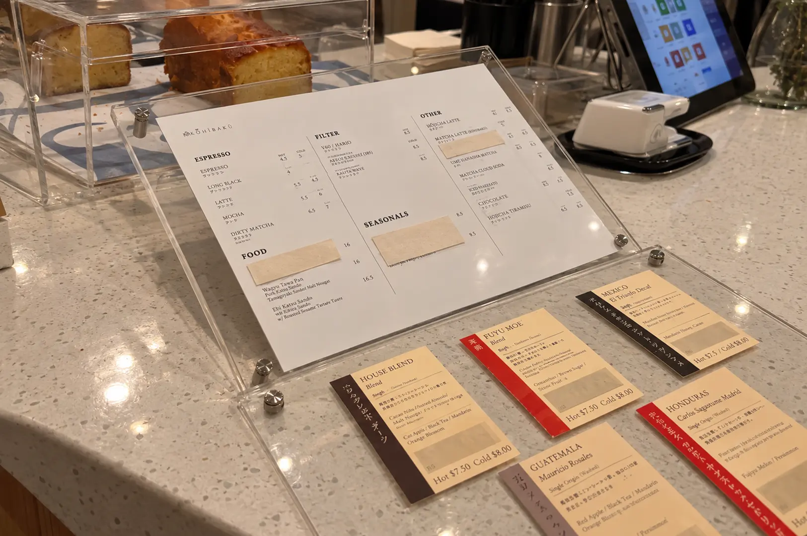 A minimalist café menu displayed beside pastries and coffee cards, showing a carefully designed menu aesthetic.