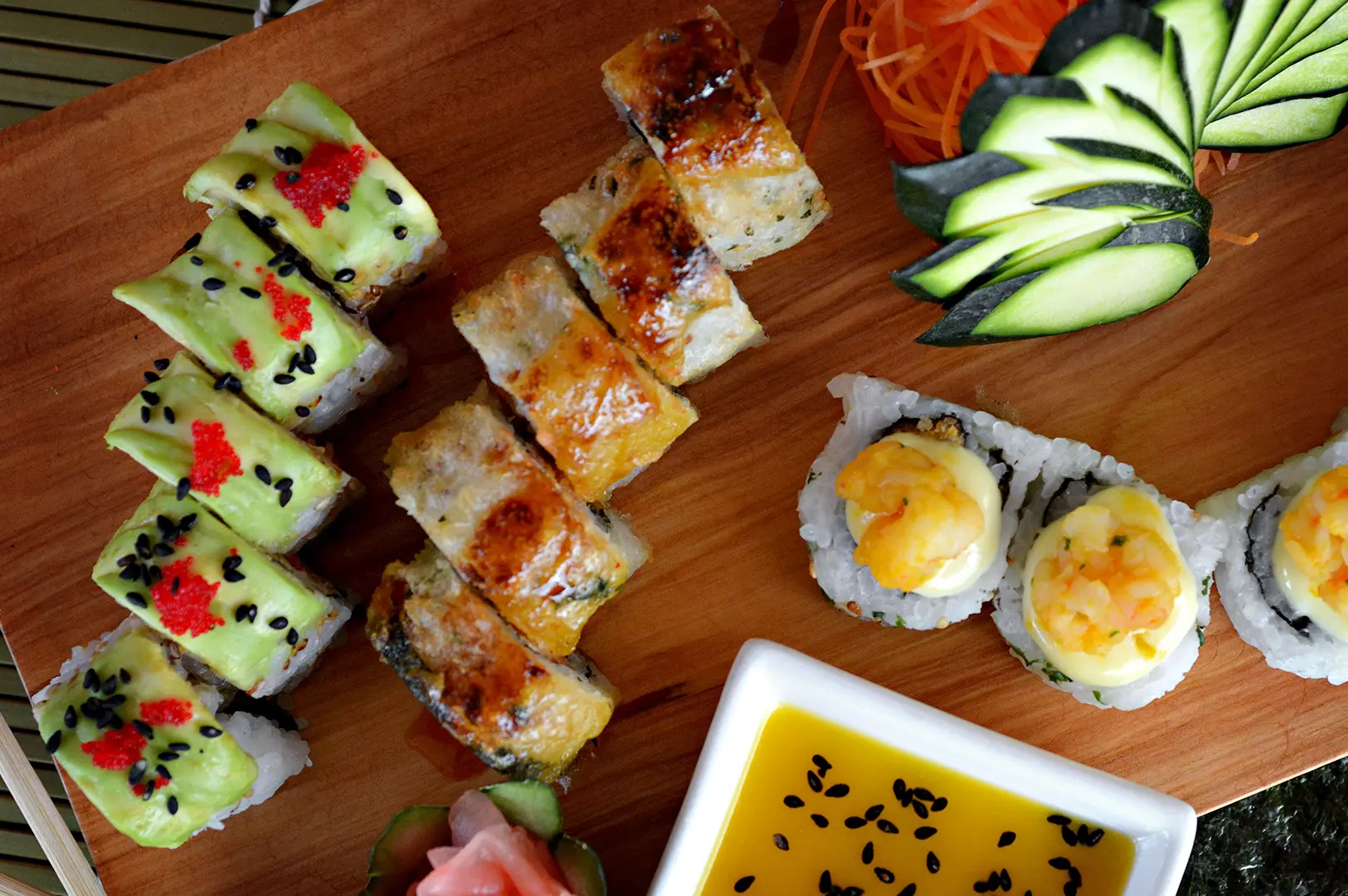Assorted sushi platter with colorful specialty rolls, nigiri, dipping sauce, and fresh vegetable garnish.