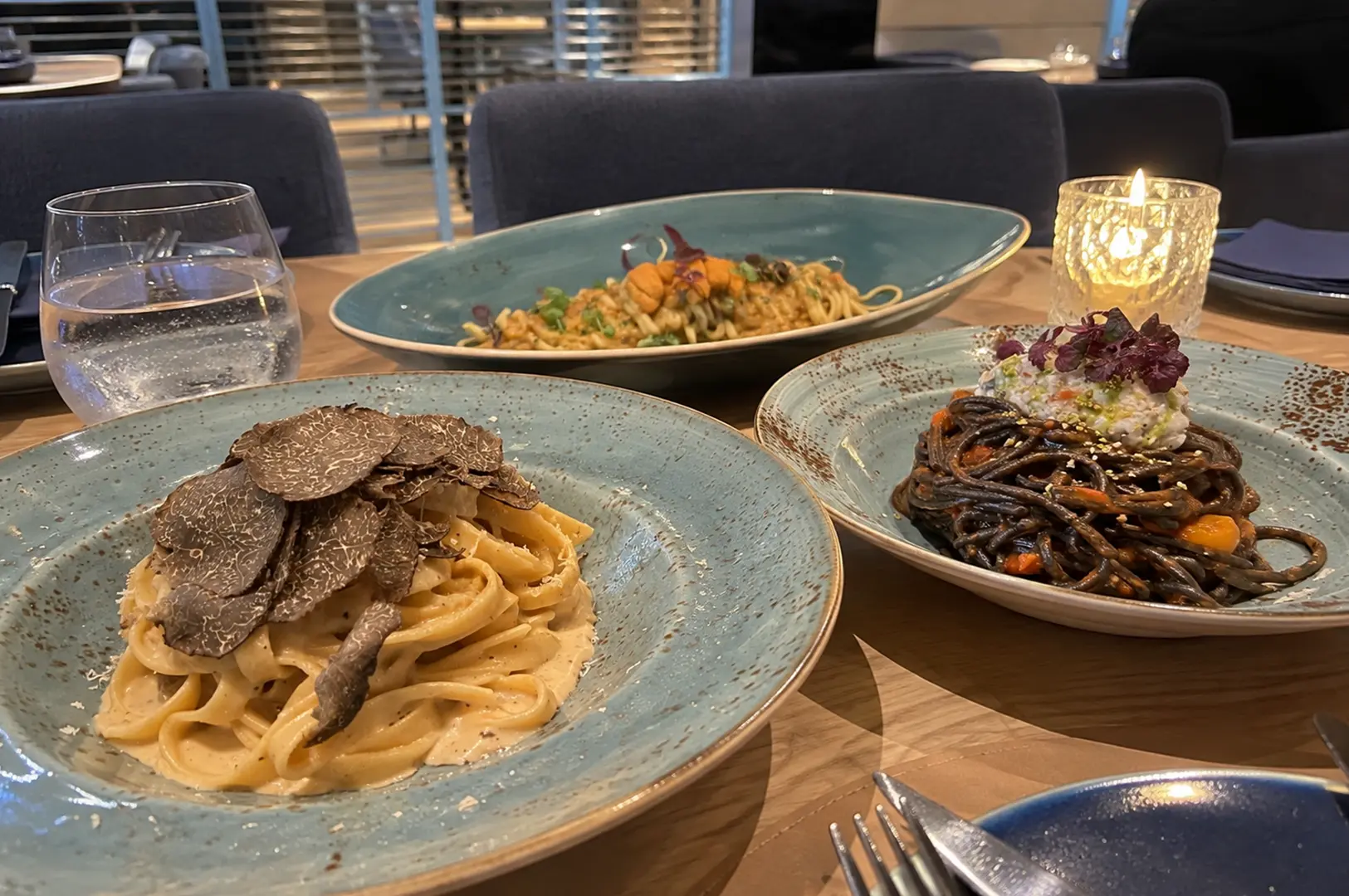 Three pasta dishes served on ceramic plates, including creamy truffle pasta and dark squid ink noodles.