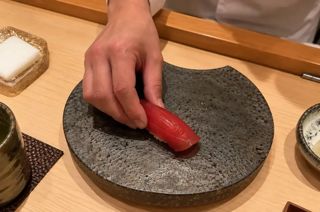 Omakase chef placing fresh tuna nigiri on a textured ceramic plate