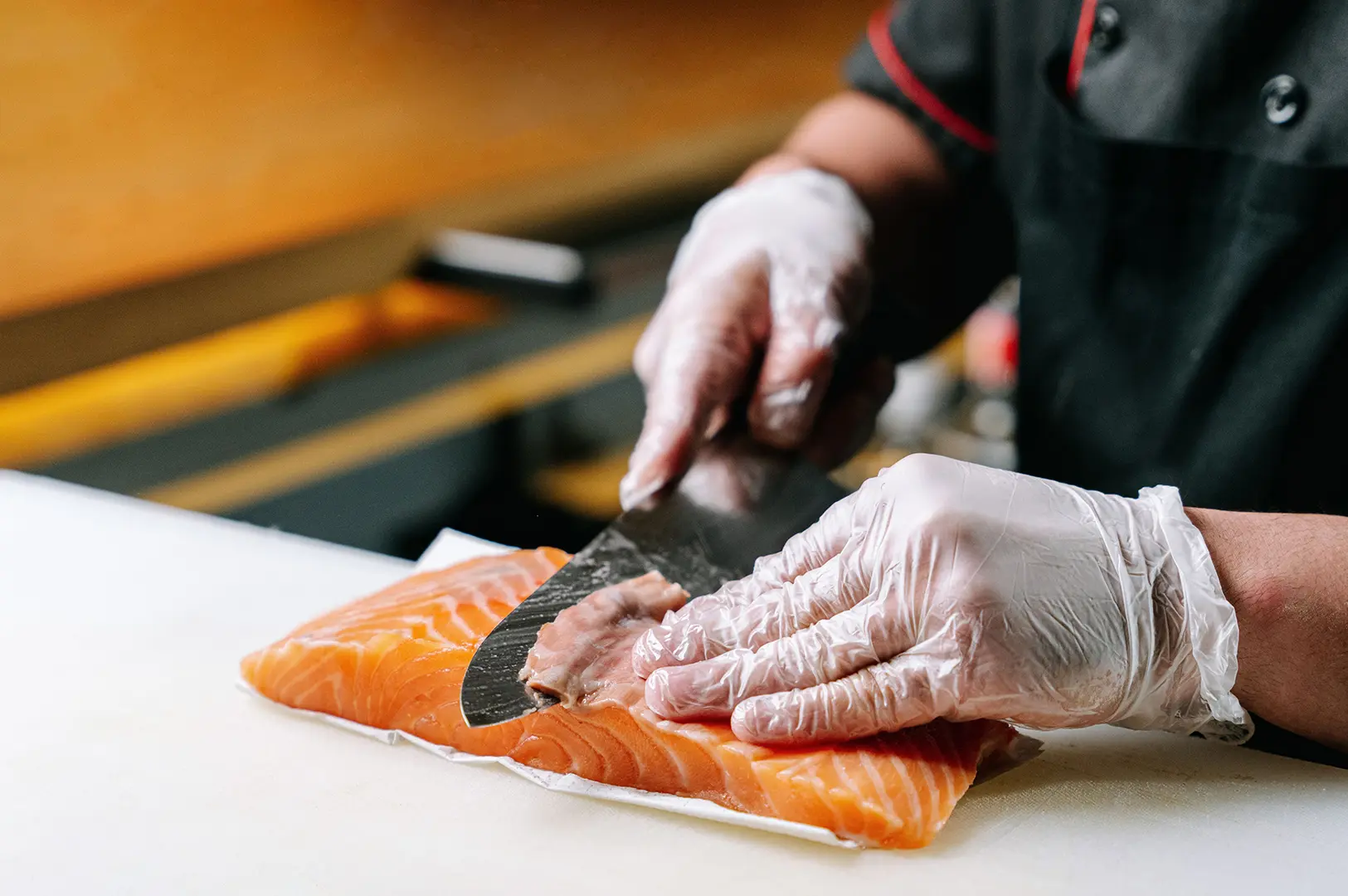 Chef slicing fresh salmon fillet with a sharp knife during sushi preparation.