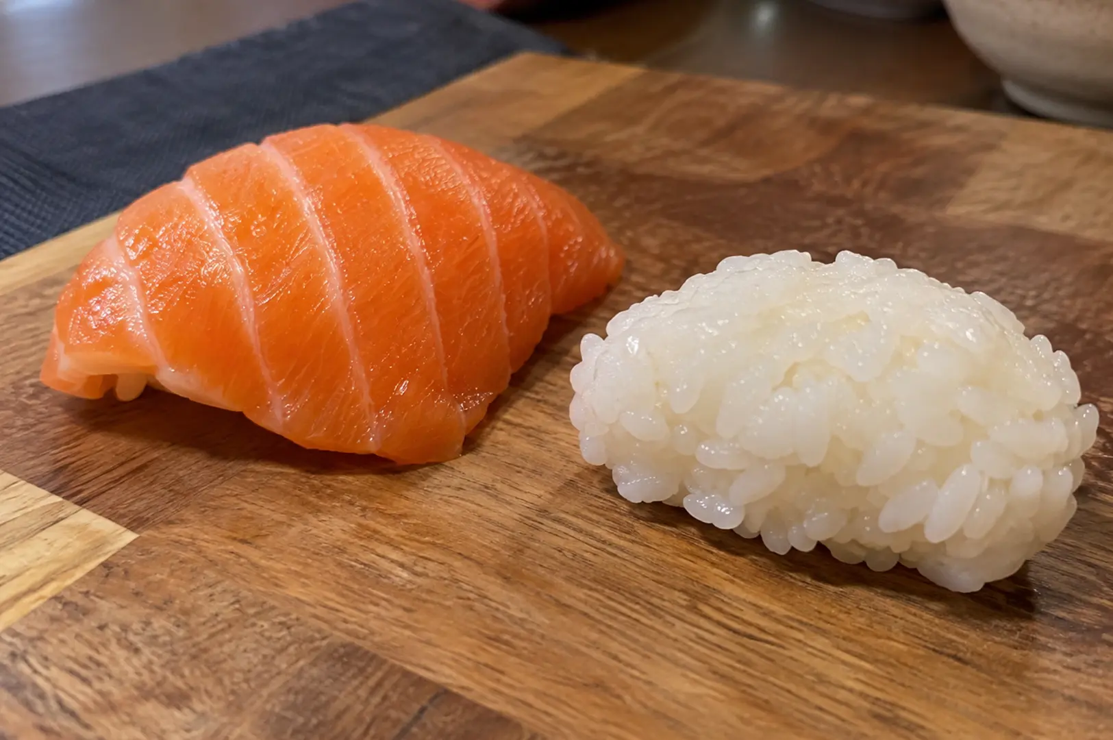 Fresh salmon nigiri beside a molded sushi rice portion on a wooden board.