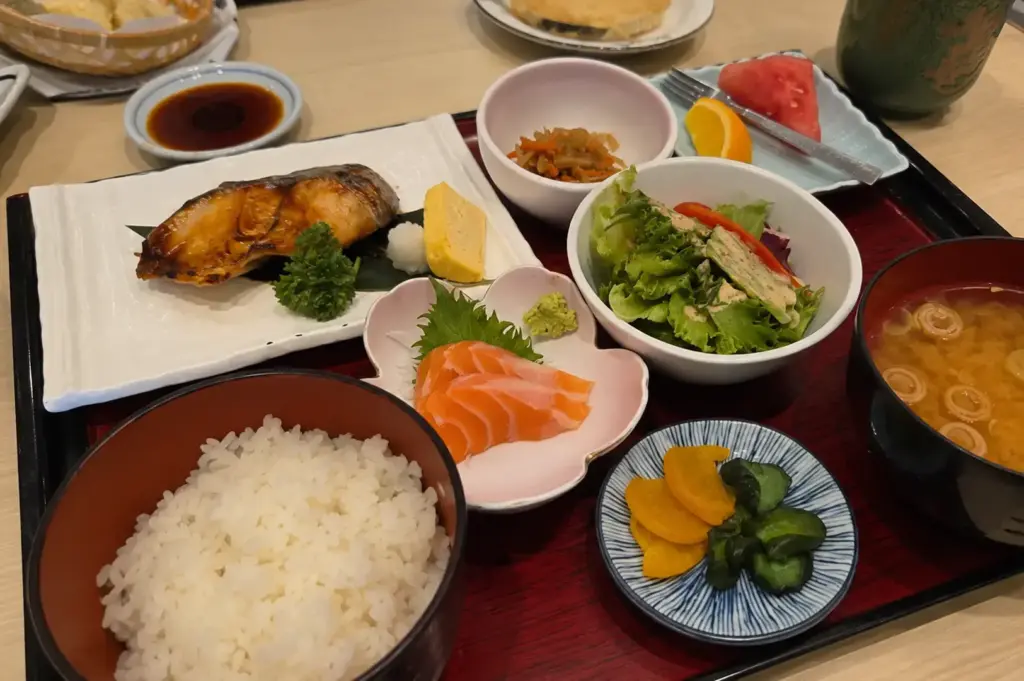 Sashi Set Lunch with grilled fish, salmon sashimi, steamed rice, miso soup, salad, and Japanese side dishes.