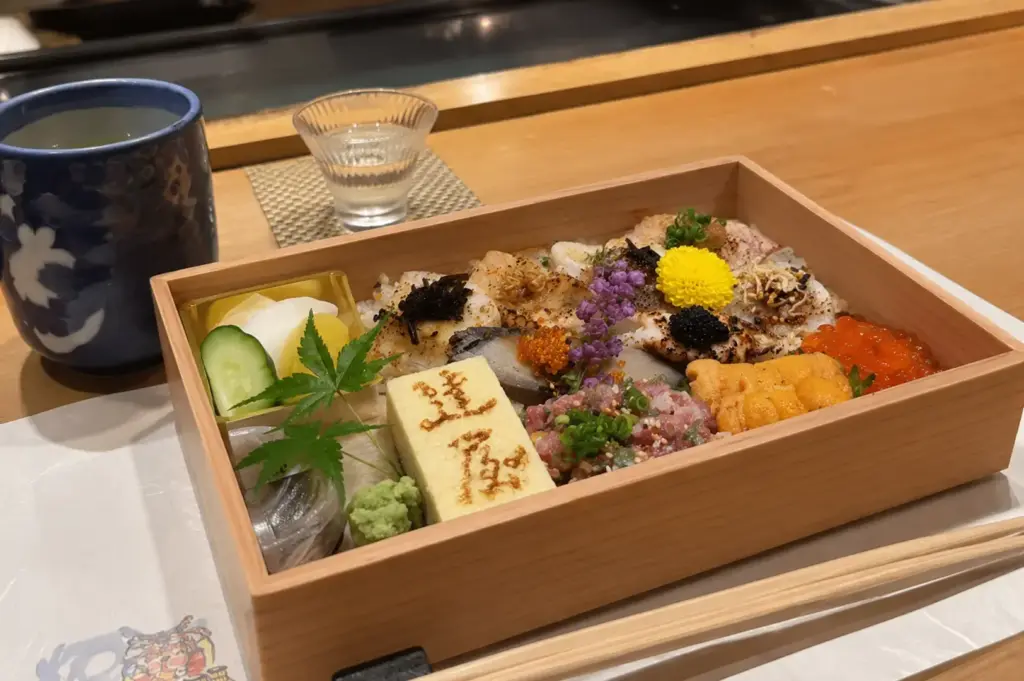 Torched Chirashizushi topped with assorted seafood, uni, ikura, tamago and garnishes in a wooden bento box
