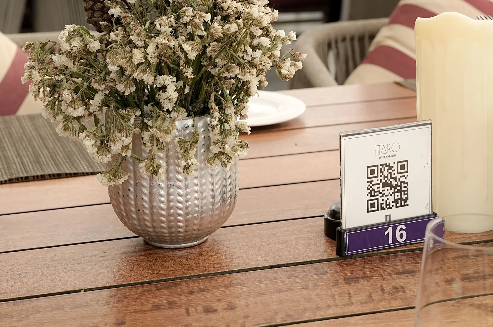 QR code menu stand on a wooden restaurant table beside a flower vase and dining tableware.