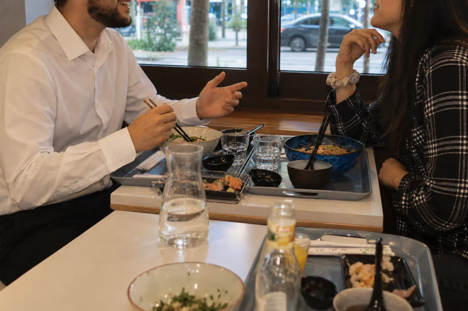 Two diners enjoying a meal together at a restaurant table with bowls, sushi, and drinks.