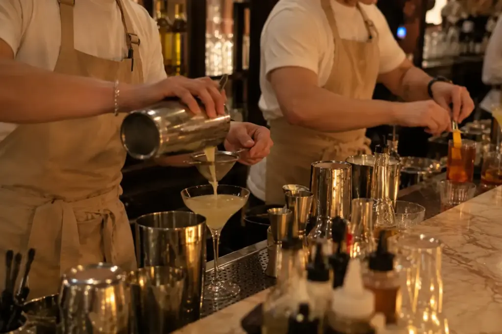 Bartenders preparing cocktails with shakers, glassware, and fresh ingredients behind the bar.