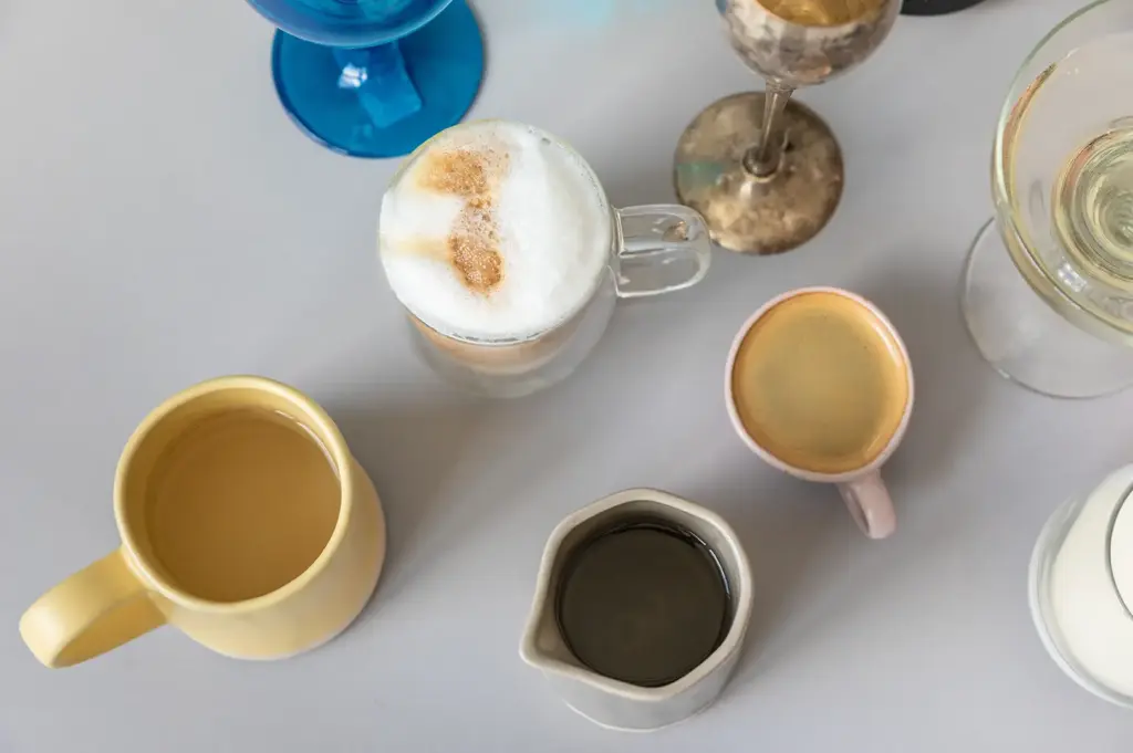 An overhead arrangement of several coffee cups and drink components displayed separately on a light café table.