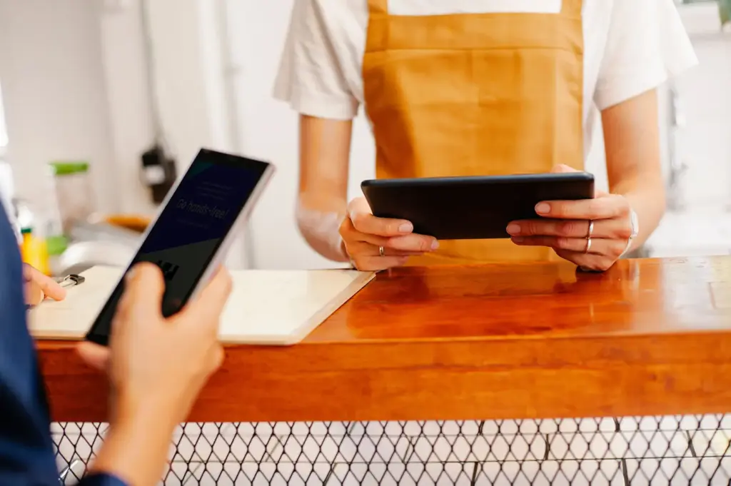 Restaurant staff holding a tablet at the counter while a customer uses a smartphone for digital ordering.