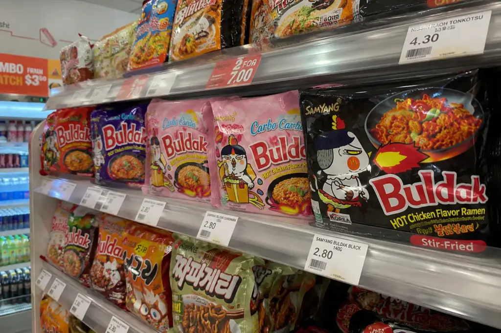 Close-up phone shot of colorful Buldak instant ramen packs neatly displayed on a convenience store shelf, highlighting the popularity of trendy Korean instant noodles.