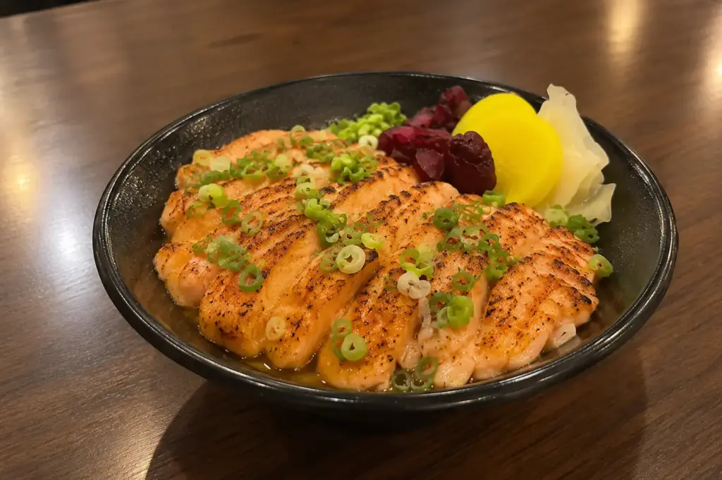 Salmon mentaiko donburi topped with seared salmon, chopped spring onions, and Japanese pickles in a black bowl.
