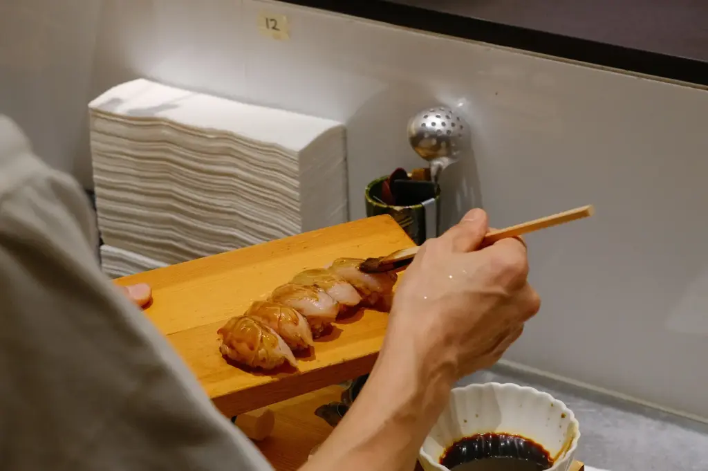 Sushi To Sumi chef presenting a wooden board of freshly prepared nigiri, with diners watching the preparation up close.