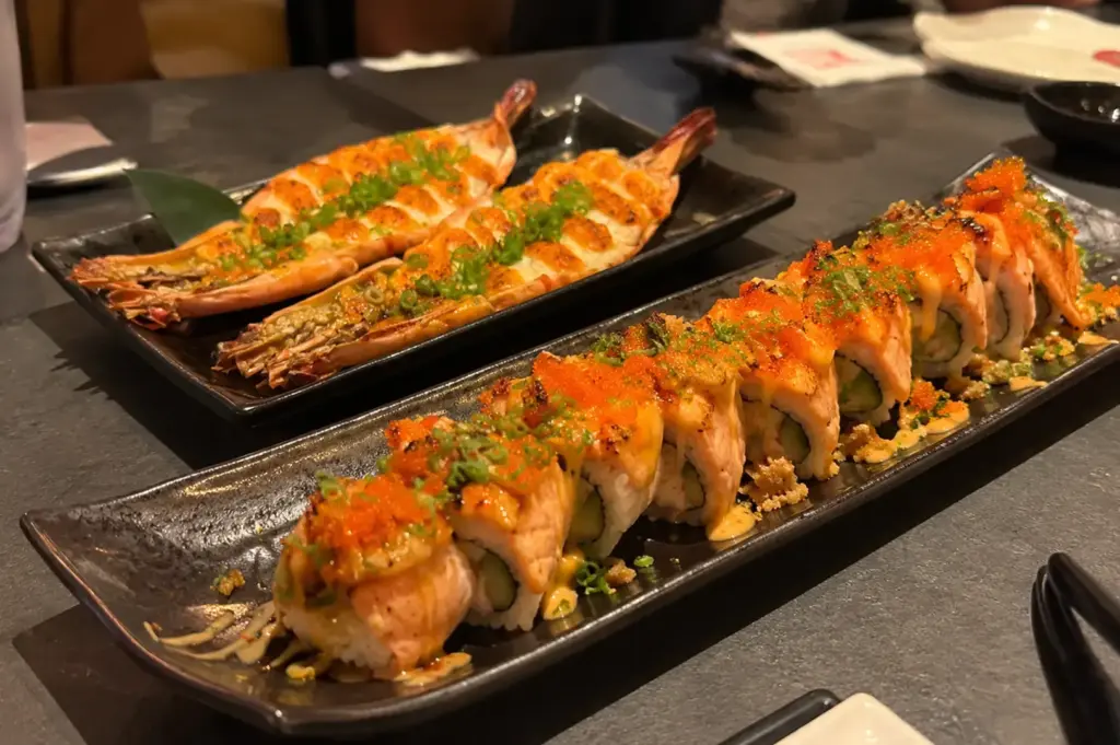 Modern sushi rolls topped with salmon, spicy roe, and green onions served with grilled prawns.