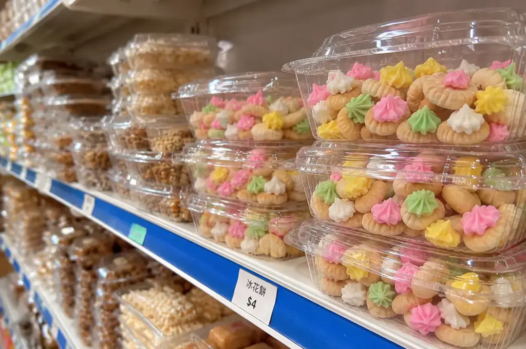 Clear plastic containers filled with colourful iced gem biscuits displayed on a shop shelf.