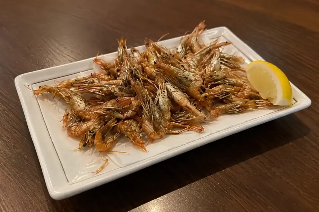 Crispy kawa ebi fried river shrimp served on a white rectangular plate with a lemon wedge.