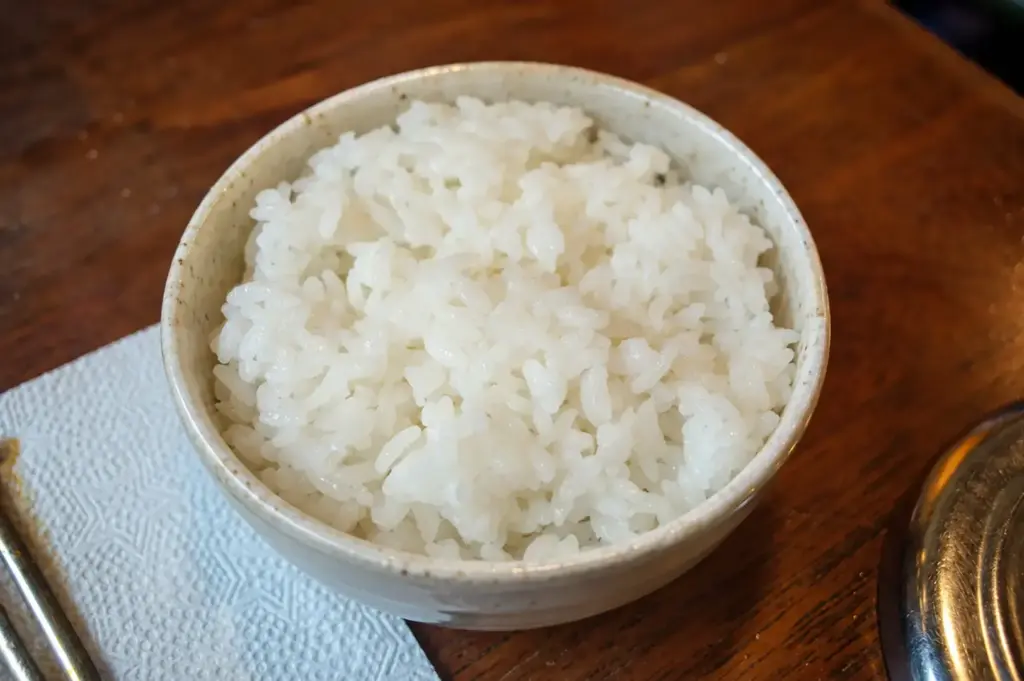 A bowl of freshly cooked white Japanese rice served on a wooden table.