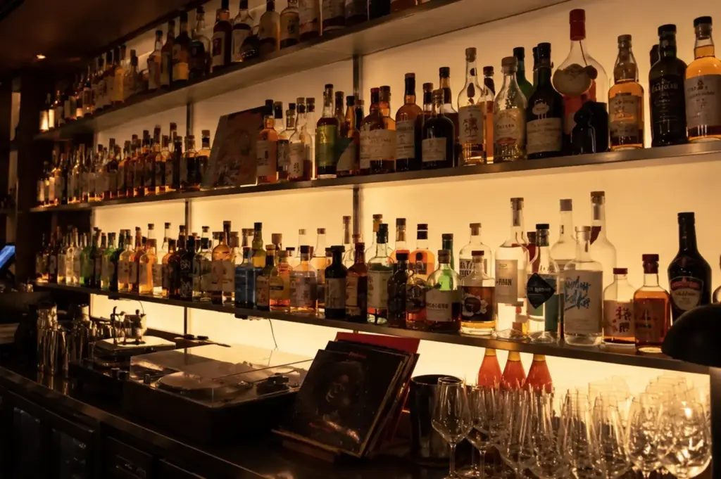 Illuminated bar shelves displaying a wide variety of liquor bottles and glassware.