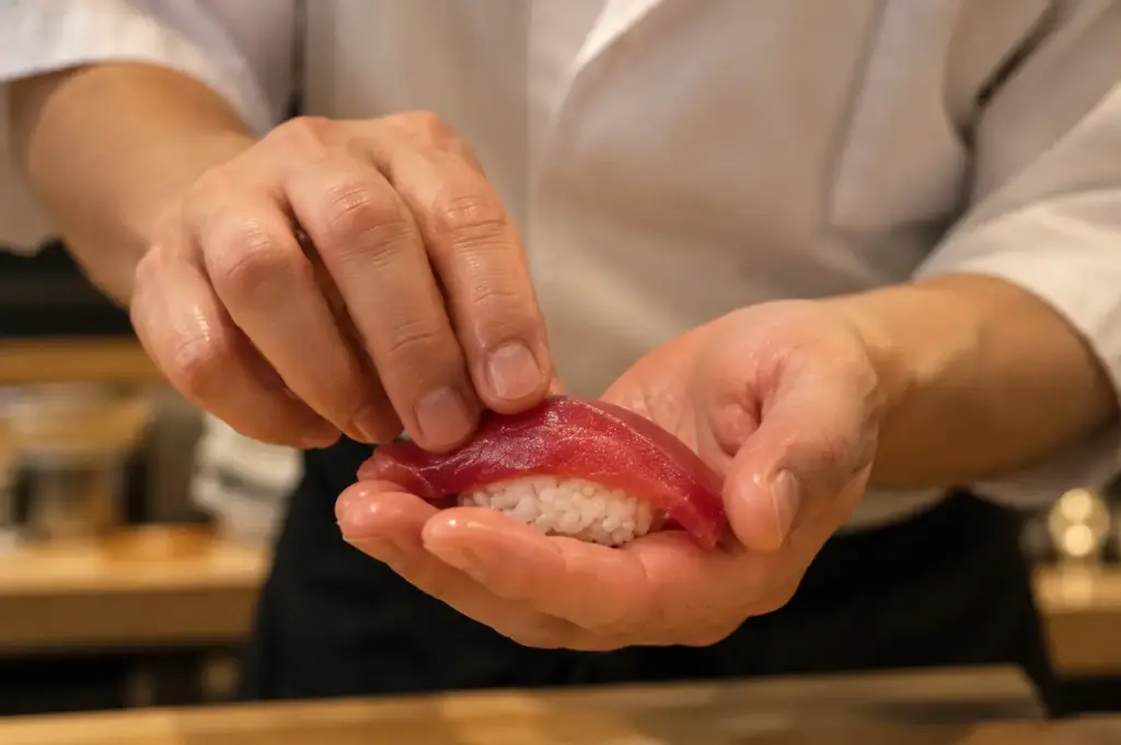 Sushi chef carefully placing a slice of tuna over a mound of rice to form nigiri.