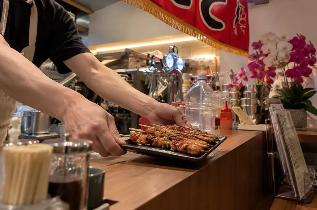 Chef serving freshly grilled yakitori across a Japanese izakaya counter.