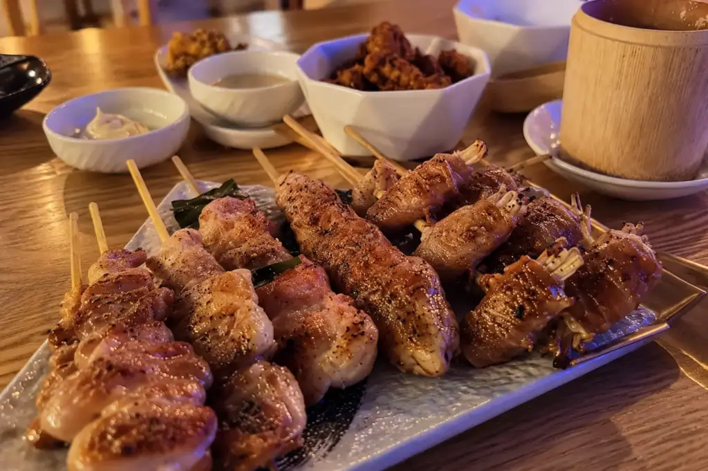 Assorted grilled yakitori skewers served on a platter at a wooden izakaya table.