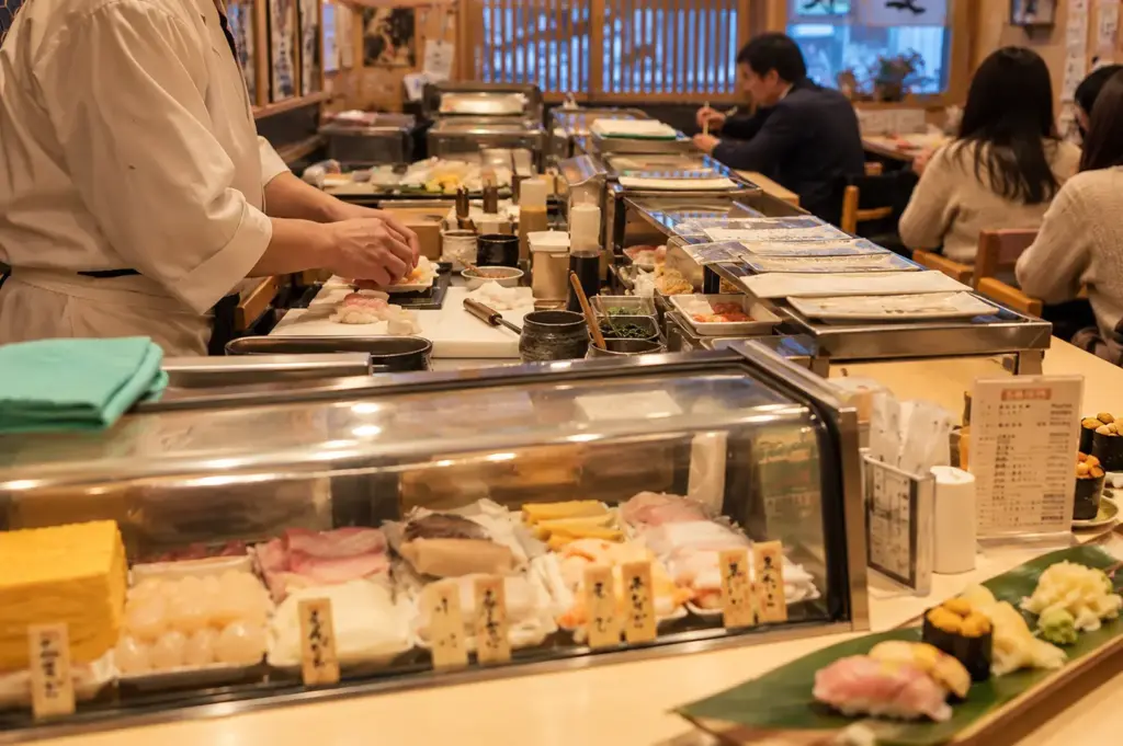 A busy Japanese sushi restaurant with a chef preparing sushi behind a long counter.