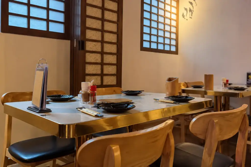 Cozy Japanese restaurant dining area with wooden tables, chopsticks, and traditional window panels.