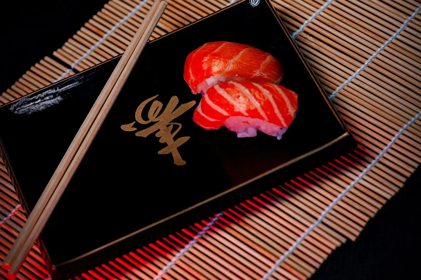 Two pieces of tuna nigiri served on a black plate with chopsticks on a traditional bamboo mat.