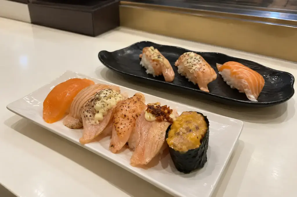 A selection of modern sushi pieces featuring salmon, seared toppings, and creative garnishes.