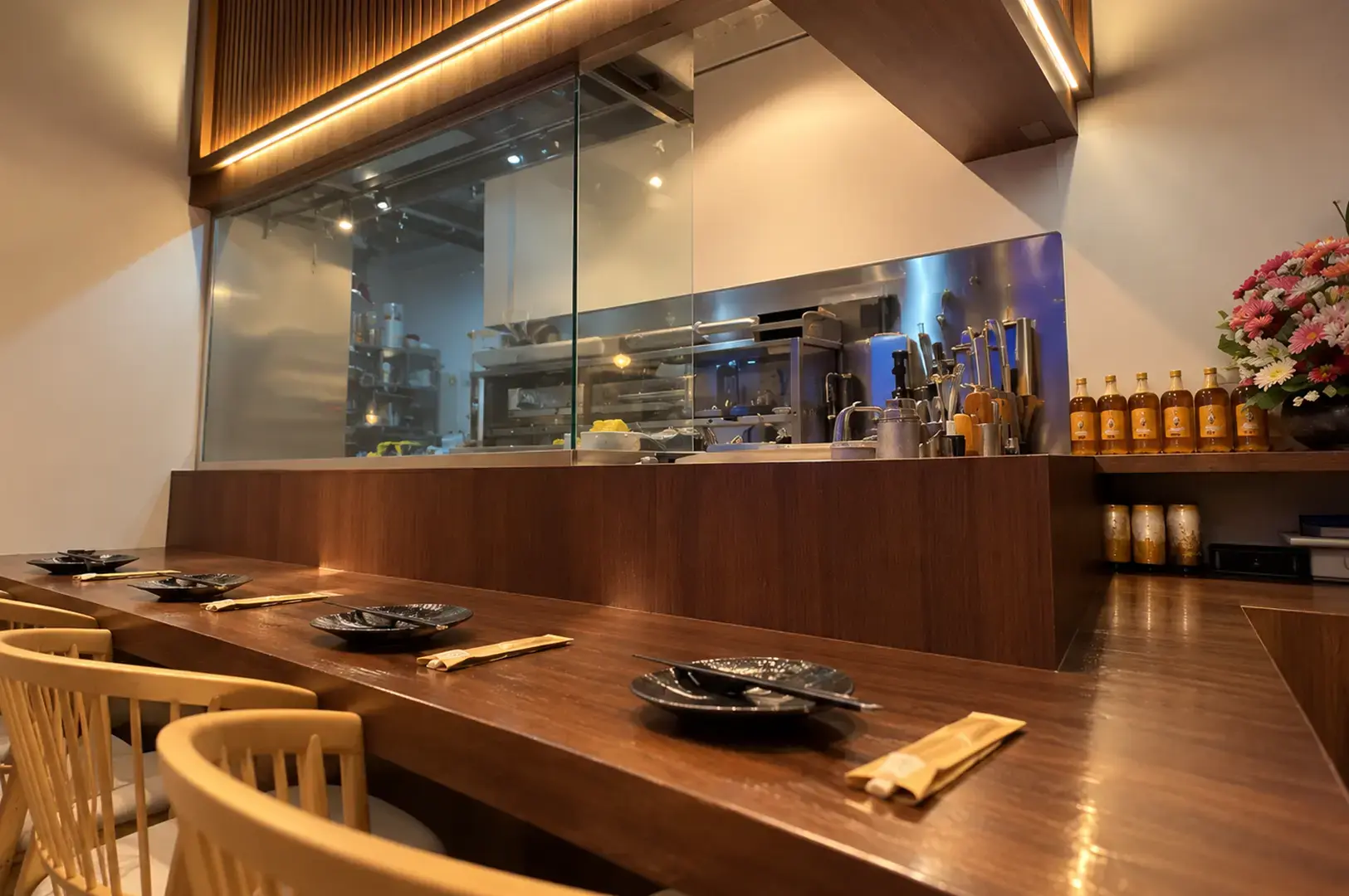Warm wooden counter and open kitchen inside a modern Japanese izakaya, set with plates and chopsticks.